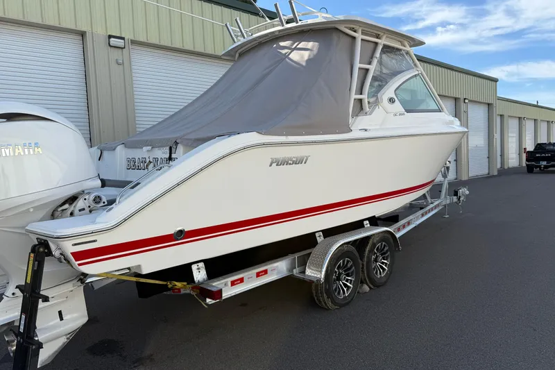 Slide: The Image of 2024 Pursuit DC 266 Dual Console boat on trailer, parked near storage units. - 49