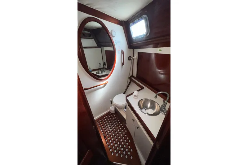 Slide: The Image of 1977 Gulfstar 50 yacht bathroom with wooden accents, round mirror, and porthole window. - 19