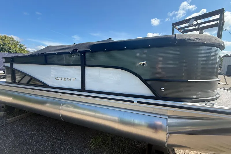 Slide: The Image of 2025 Crest Classic 200 pontoon boat with sleek design, parked outdoors under blue sky. - 2