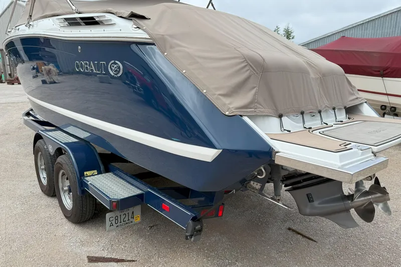 Slide: The Image of 2016 Cobalt 26SD boat on trailer, covered, with dual propellers, parked outdoors. - 2