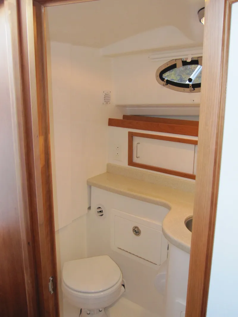 Slide: The Image of 2011 Back Cove 30 boat bathroom with wooden trim, compact toilet, and small sink. - 14