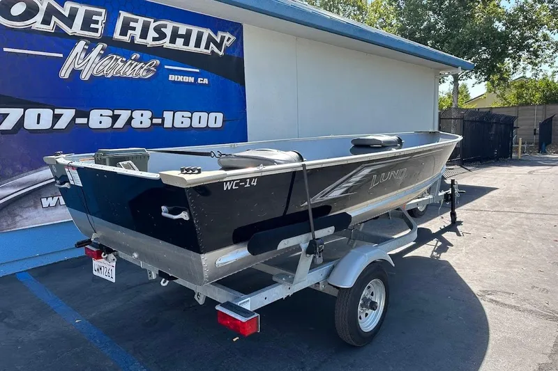 Slide: The Image of 2024 Lund WC-14 boat on trailer outside marine shop, sunny day. - 5