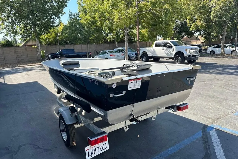 Slide: The Image of 2024 Lund WC-14 boat on trailer in parking lot, surrounded by trees and vehicles. - 7