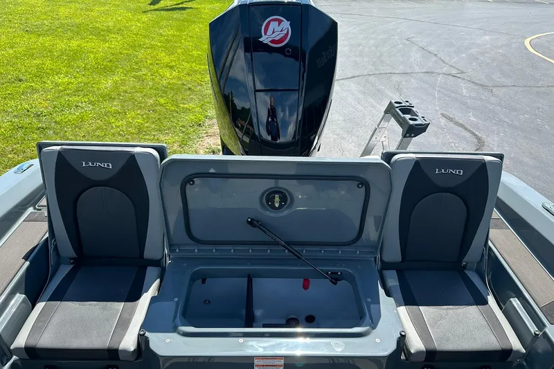Slide: The Image of 2026 Lund 185 Impact GL boat interior with seating and motor, parked on grass. - 12