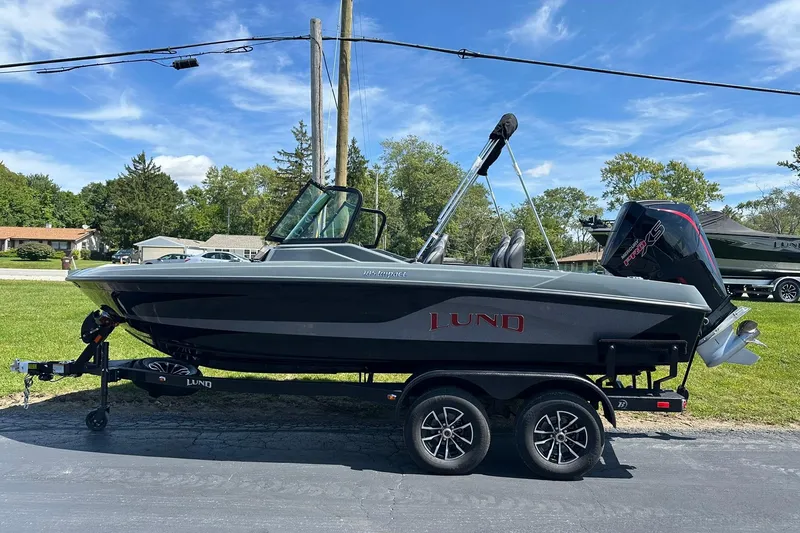 Slide: The Image of 2026 Lund 185 Impact GL boat on trailer, parked outdoors under a clear blue sky. - 4