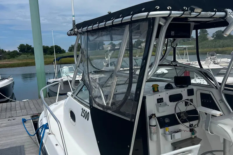 Slide: The Image of 2002 Angler 2500 WA boat docked, featuring a covered helm and modern controls. - 4