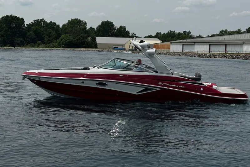 Slide: The Image of 2026 Crownline 298 SS boat cruising on a calm lake near a marina. - 1