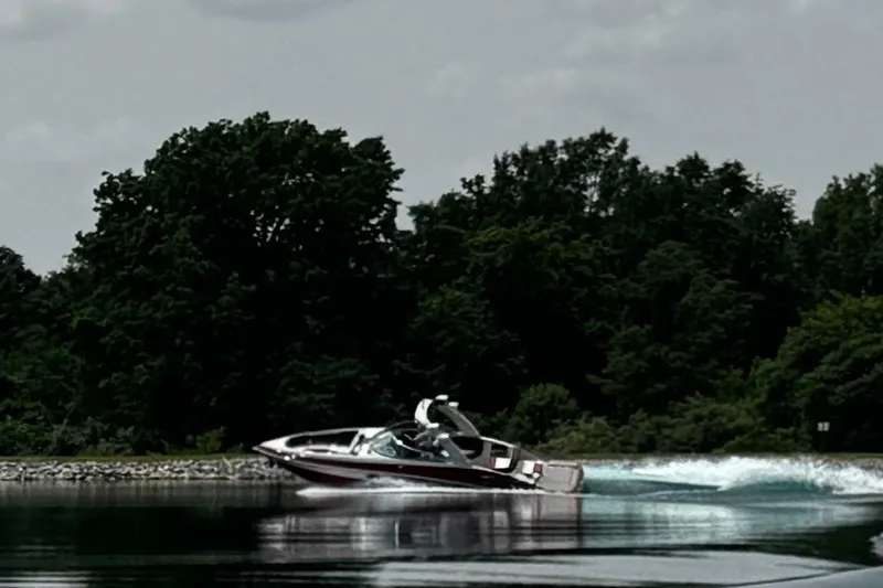 Slide: The Image of 2026 Crownline 298 SS speedboat cruising on a serene lake with lush green trees. - 2