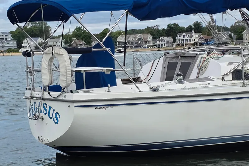 Slide: The Image of 1987 Catalina 30 MkII sailboat docked near coastal homes, featuring blue canopy. - 1
