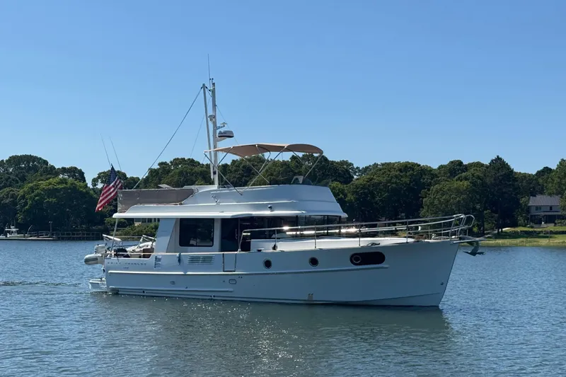 The Image of 2018 Beneteau Swift Trawler 44 cruising on a serene lake with lush greenery. - 0