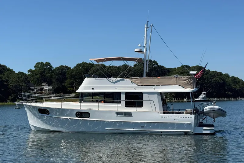 Slide: The Image of 2018 Beneteau Swift Trawler 44 on calm water, side view with clear sky. - 2