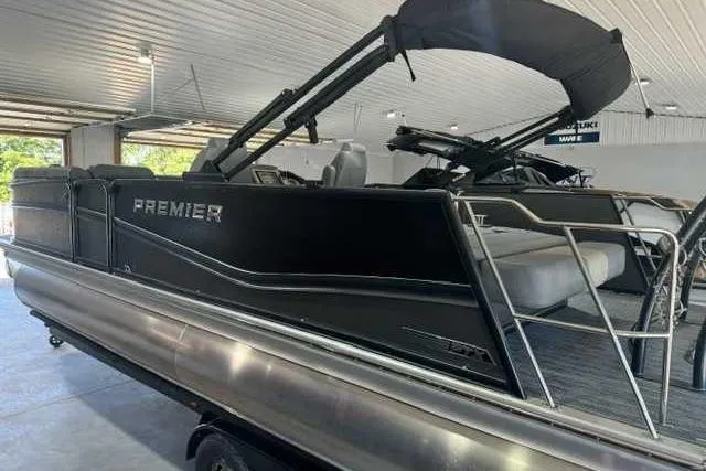 Slide: The Image of 2024 Premier 250 Intrigue RL pontoon boat in a showroom, featuring sleek black design. - 10