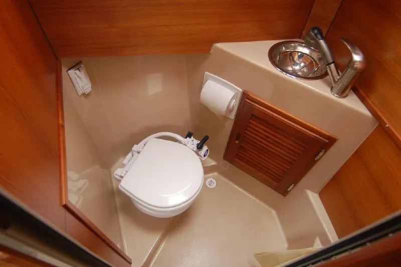 Slide: The Image of 2016 Ranger Tugs R25 SC boat bathroom with toilet, sink, and wooden cabinetry. - 13