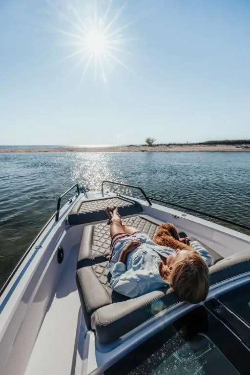 Slide: The Image of Person relaxing on Axopar 37XC boat under sunny sky, near a serene shoreline. - 4
