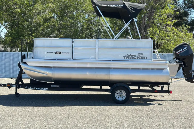 The Image of 2026 Sun Tracker Party Barge 16 DLX pontoon boat on trailer, parked outdoors. - 1