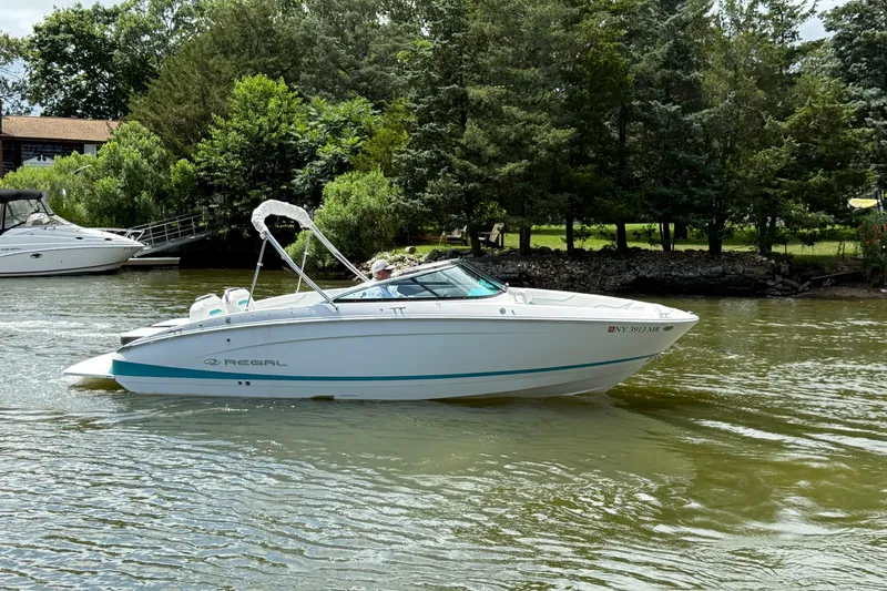 Slide: The Image of 2020 Regal LS4 boat cruising on a scenic lake with lush greenery. - 1