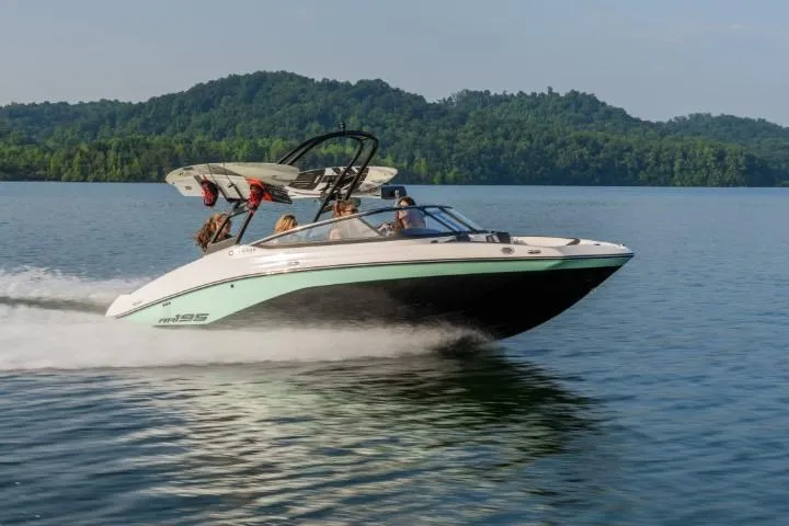 The Image of 2026 Yamaha Boats AR195 speeding on a lake with lush green hills in the background. - 0