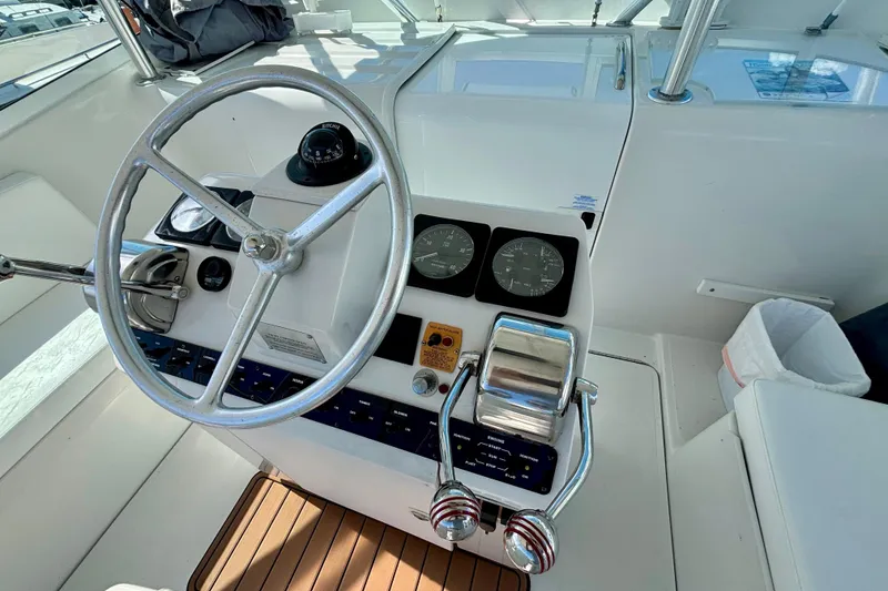 Slide: The Image of 2002 Luhrs 32 Open helm with steering wheel, gauges, and controls on teak flooring. - 23