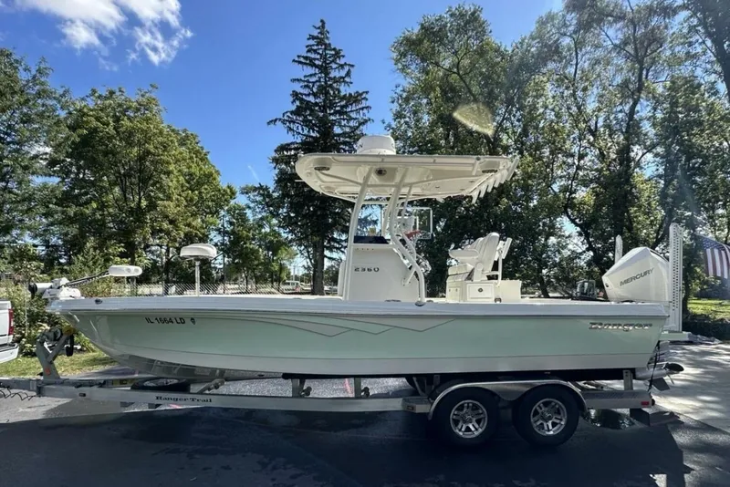 The Image of 2022 Ranger 2360 Bay boat on trailer, parked outdoors under clear blue sky. - 0