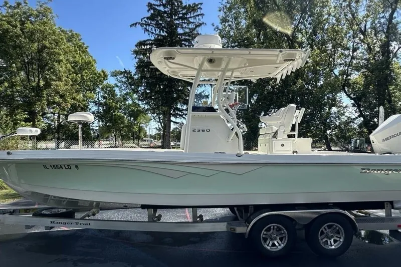 Slide: The Image of 2022 Ranger 2360 Bay boat on trailer, parked outdoors with trees in background. - 12