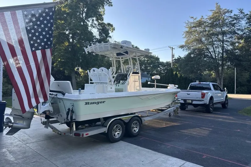 Slide: The Image of 2022 Ranger 2360 Bay boat with Mercury engine, parked on trailer, surrounded by trees. - 6