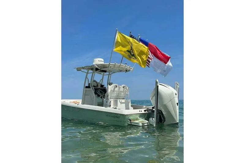Slide: The Image of 2022 Ranger 2360 Bay boat with flags, on calm water near a forested shoreline. - 8
