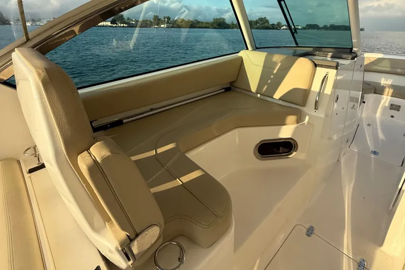 Slide: The Image of 2016 Pursuit DC 325 Dual Console interior with beige seating, overlooking calm waters. - 21