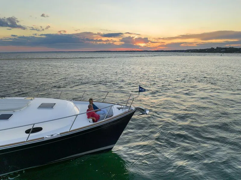 Slide: The Image of 2023 Eastbay EB60 yacht cruising near coastal homes, American flag displayed. - 14