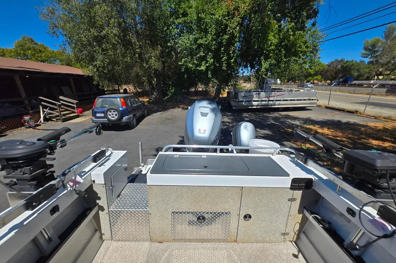 Slide: The Image of 2021 Raider 210.Explorer boat with motor, parked outdoors near trees and vehicles. - 7