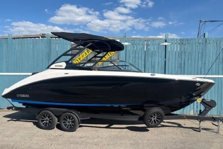 The Image of 2026 Yamaha Boats 252SD on trailer, sleek black design, parked outdoors under blue sky. - 0