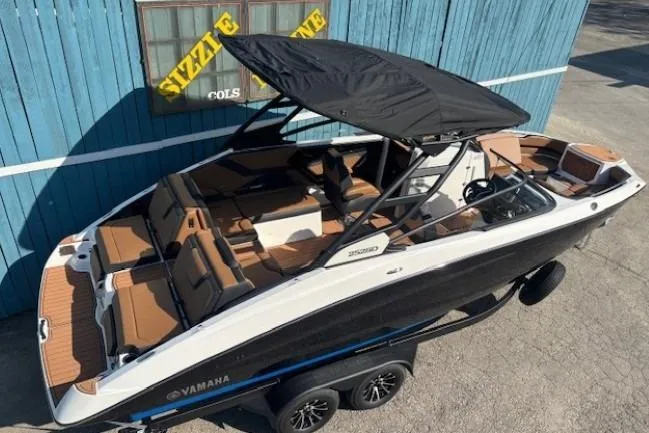 Slide: The Image of 2026 Yamaha Boats 252SD with canopy, parked on trailer, blue building background. - 6