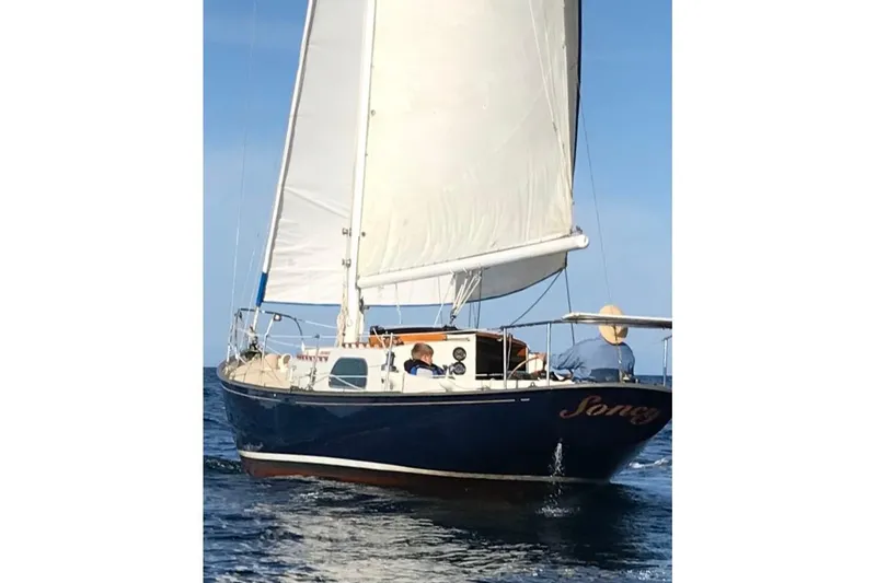 Slide: The Image of 1957 Rhodes Bounty sailboat with white sails on open water. - 2