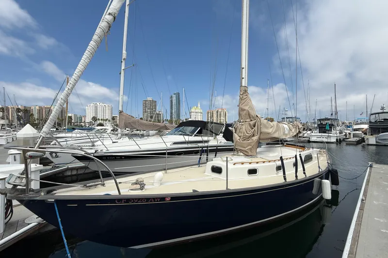 Slide: The Image of 1957 Rhodes Bounty sailboat docked in marina with city skyline background. - 4