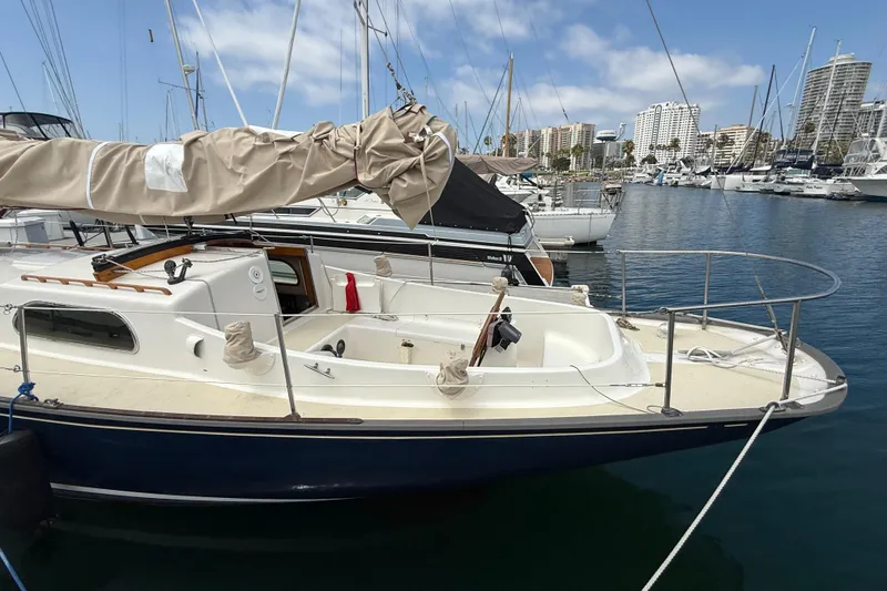 Slide: The Image of 1957 Rhodes Bounty sailboat docked in marina, surrounded by other boats and city skyline. - 5
