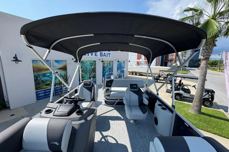 Slide: The Image of 2026 Bennington 22 SSB pontoon boat with canopy, parked near a building and palm trees. - 22