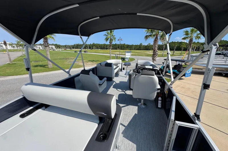 Slide: The Image of 2026 Bennington 22 SSB pontoon boat interior with seating and canopy, parked near palm trees. - 34