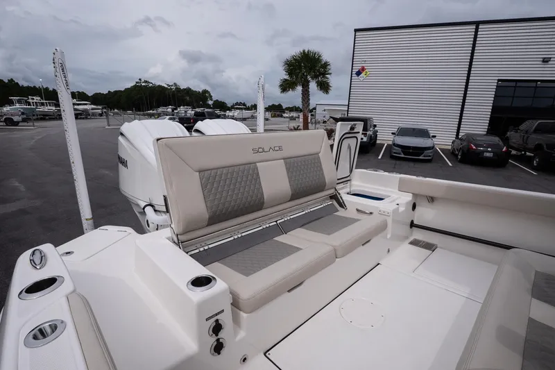 Slide: The Image of 2026 Solace 28 HCS boat with cushioned seating, parked near a modern building. - 17