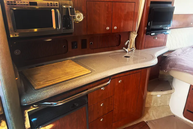 Slide: The Image of 2006 Sea Ray 320 Sundancer interior kitchen with wood cabinetry, microwave, and sink. - 8