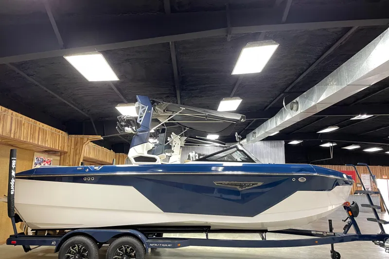 The Image of 2025 Nautique Super Air Nautique S23 boat displayed indoors on a trailer. - 1