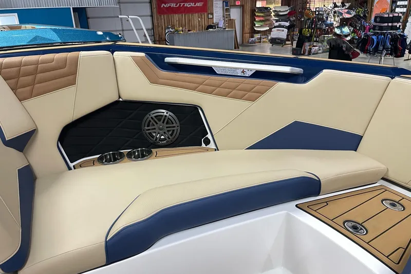 Slide: The Image of 2025 Nautique Super Air Nautique S23 interior with beige and blue seating, cup holders, and speaker. - 5