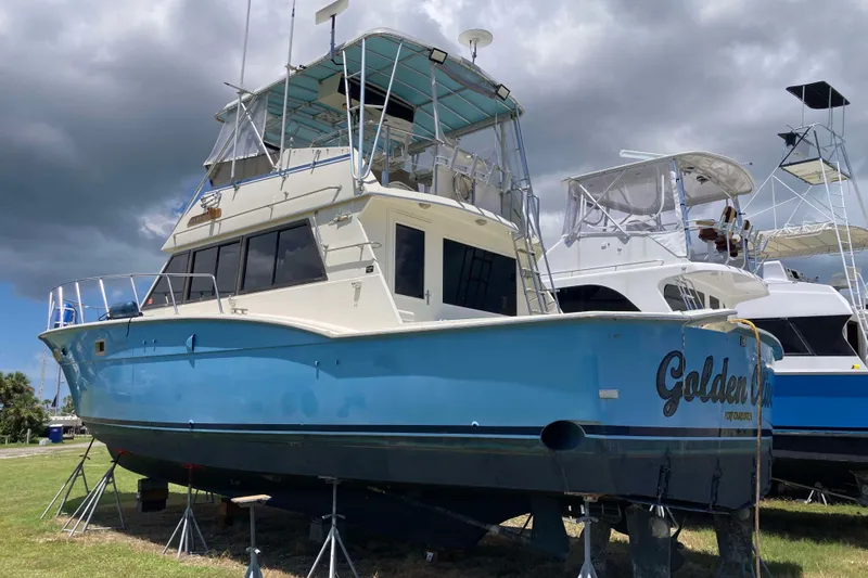 The Image of 1985 Hatteras Sportfish boat on stands, blue hull, cloudy sky background. - 0