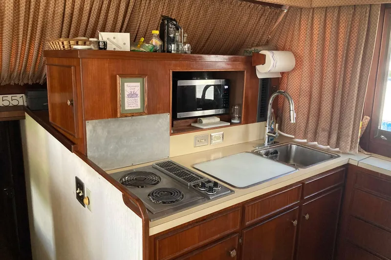 Slide: The Image of 1985 Hatteras Sportfish kitchen with stove, microwave, sink, and wooden cabinetry. - 27