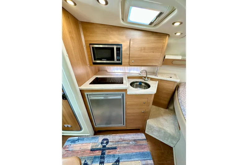 Slide: The Image of 2015 Rinker 340 Express Cruiser interior kitchen with microwave, sink, and compact fridge. - 20