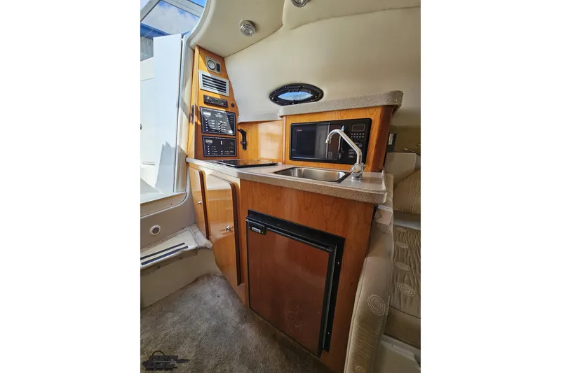 Slide: The Image of 2003 Regal Commodore 2665 boat interior with kitchenette, featuring sink, microwave, and wood cabinetry. - 57