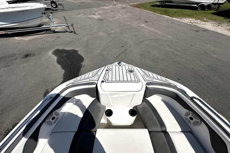 Slide: The Image of 2020 Yamaha Boats SX210 bow area with seating and cup holders, parked on pavement. - 23