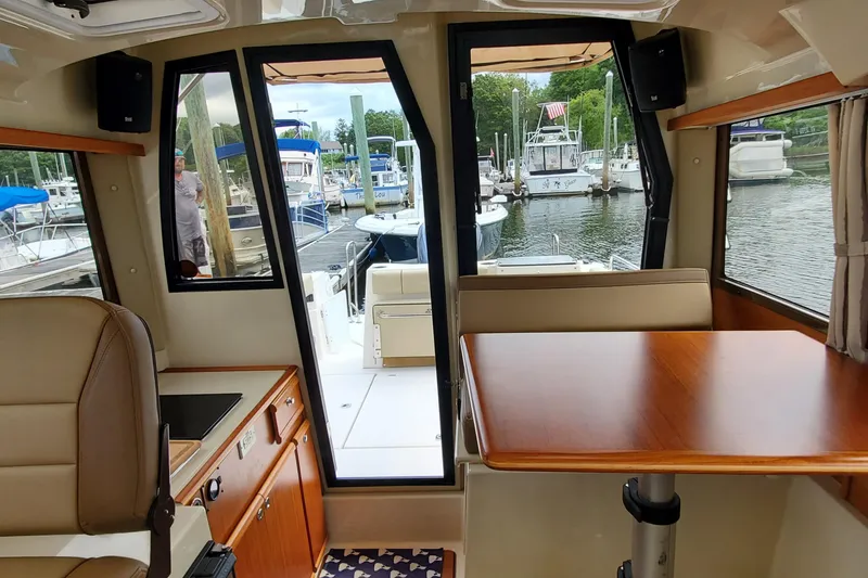 Slide: The Image of Interior view of 2021 Ranger Tugs R-25 boat, featuring a cozy dining area and marina backdrop. - 20