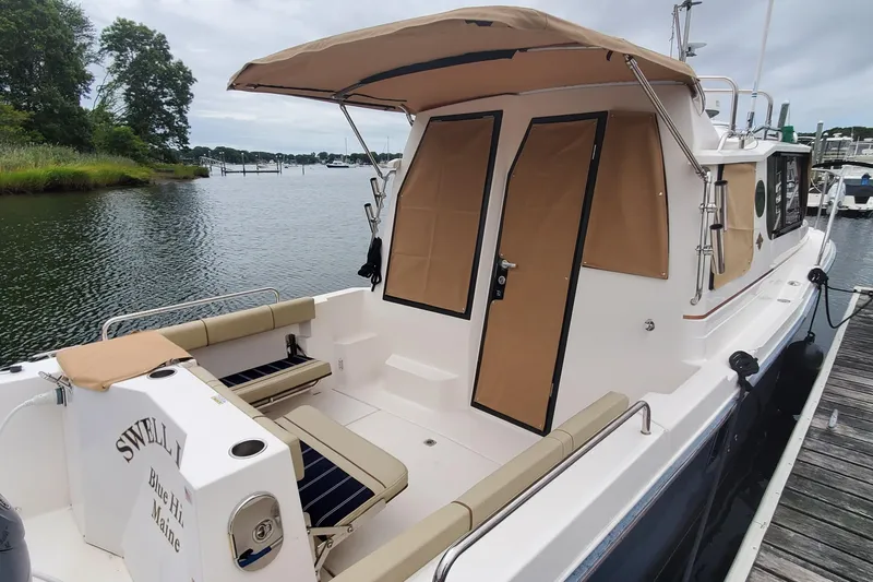 Slide: The Image of 2021 Ranger Tugs R-25 boat docked, featuring tan canopy and seating, scenic waterfront view. - 7