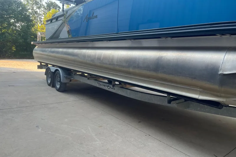 Slide: The Image of 2023 Avalon LSZ 2585 QL pontoon boat on trailer, parked outdoors. - 2
