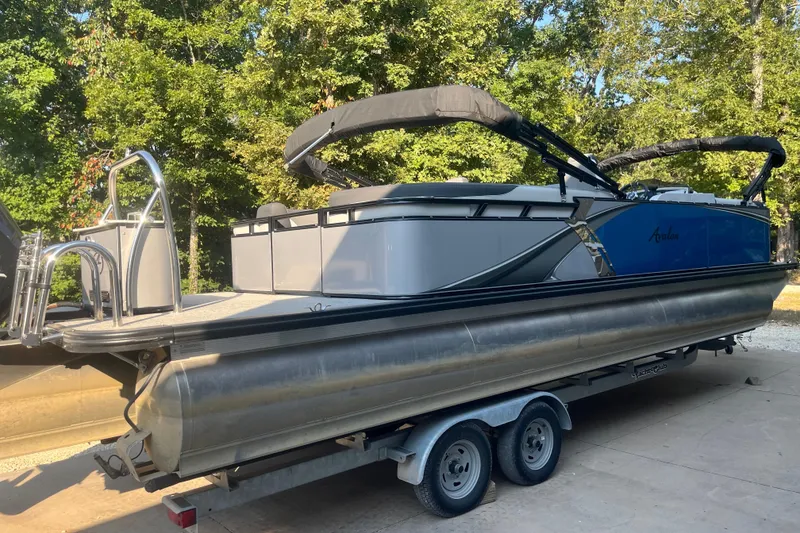 Slide: The Image of 2023 Avalon LSZ 2585 QL pontoon boat on trailer, surrounded by trees. - 3