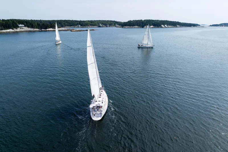 Slide: The Image of Sailboats on open water, featuring a 2024 Outbound 46 model, near a forested coastline. - 4